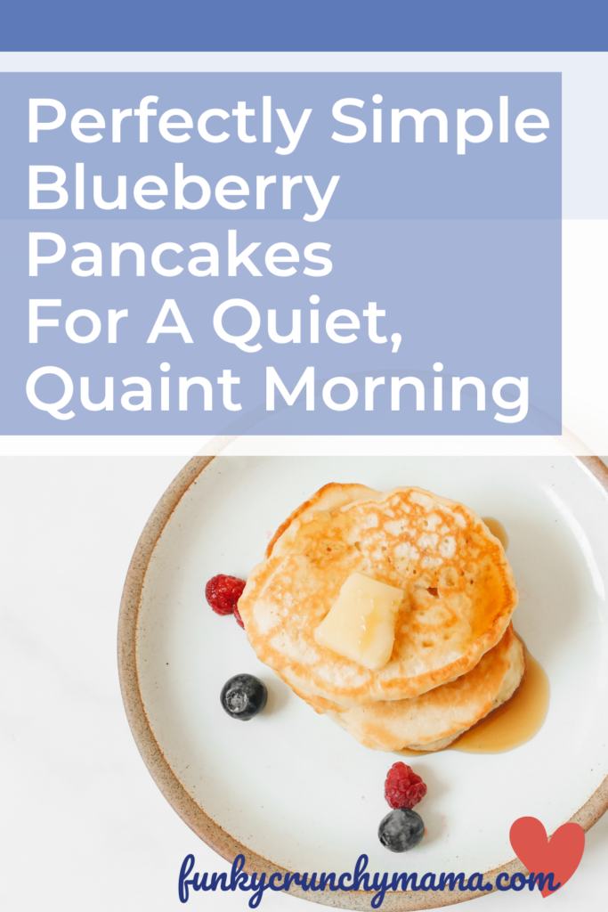 Pinterest optimized image includes photo of fluffy pancakes on a pottery plate with berries. Image is over a blue background with article title, "Perfectly Simple Blueberry Pancakes For A Quiet, Quaint Morning" in a beige box with white text. Website URL, funkycrunchymama.com is included along the bottom.