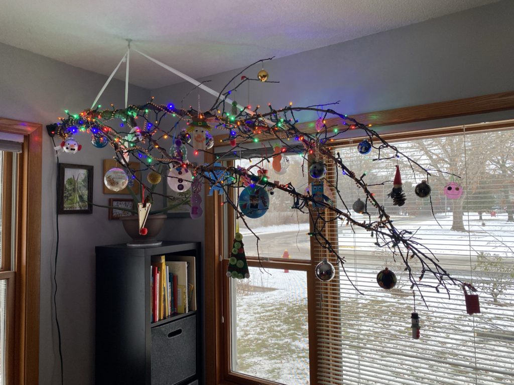Photo of  a decorated tree branch with multi-colored lights and many handmade ornaments.