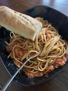 A bowl full of spaghetti covered in meatless spaghetti sauce and accompanied by a baguette.